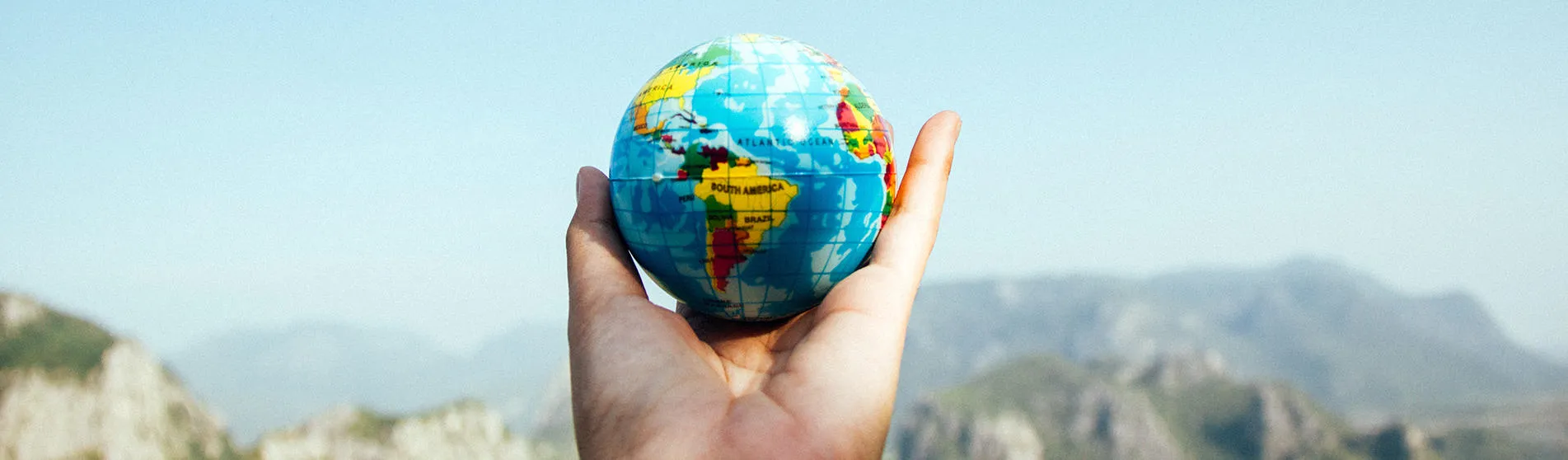A hand holding a small globe of the earth.