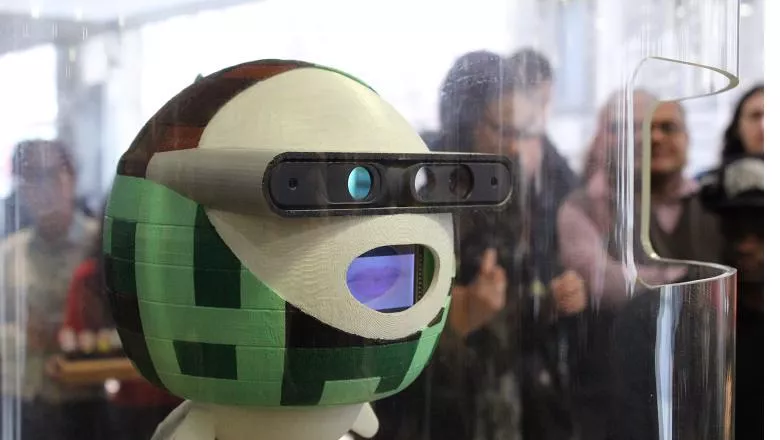 Kinba, robot receptionist. Circular green robot with, eye cameras and mouth on a screen.