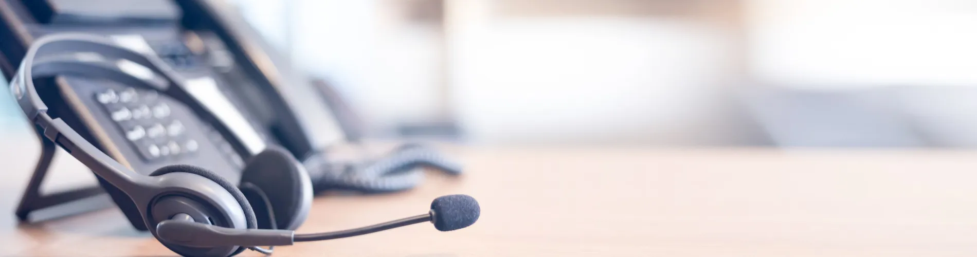 Close-up of a headset resting on a desk next to an office phone, symbolizing customer service or support services.