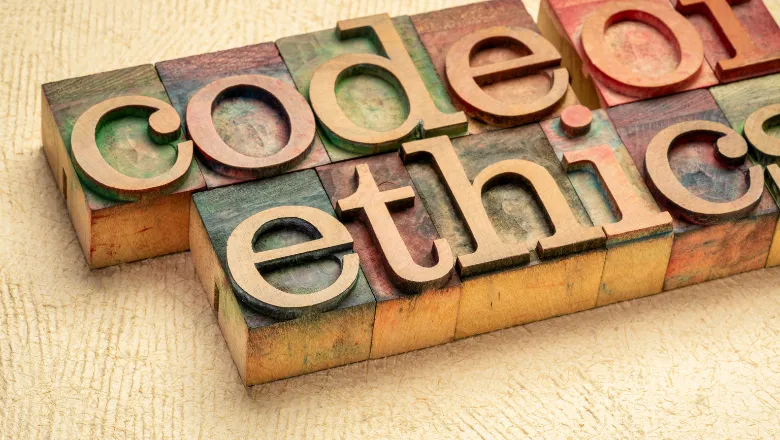 wooden printing blocks in green, purple and red, arranged on a wooden table to spell code of ethics