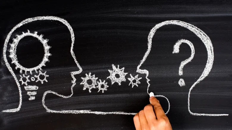 Two head profiles drawn out with a hand in chalk, one has cogs, the other a question mark.