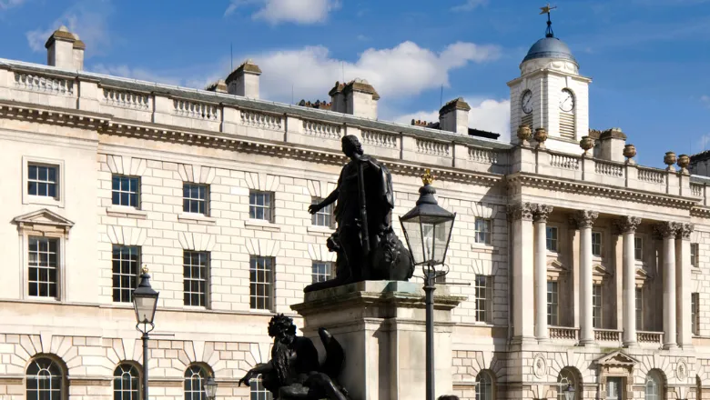 An exterior shot of Somerset House East Wing - an old, white stone building - with a statue in the foreground 