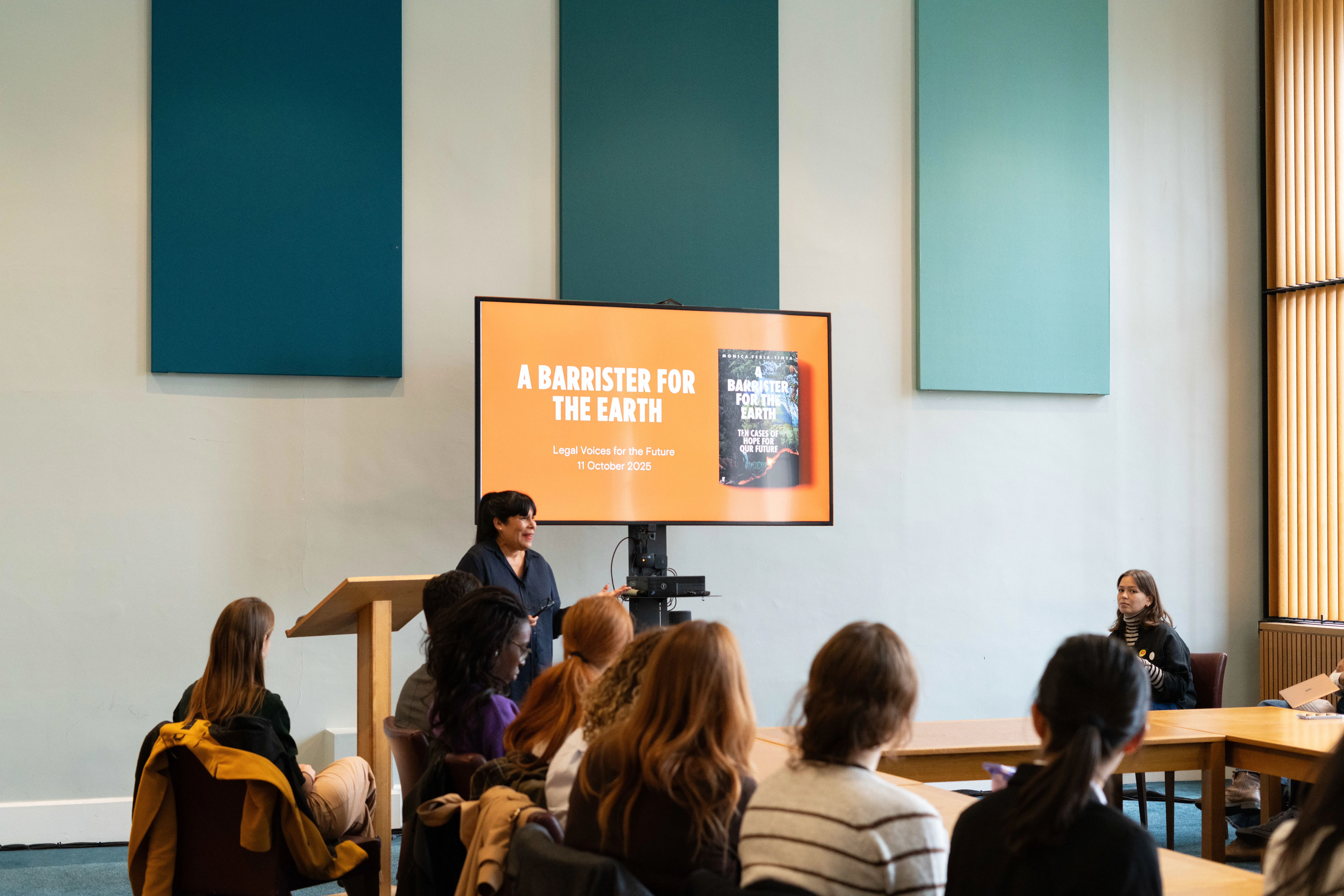 Audience watching a woman speak in front of a screen