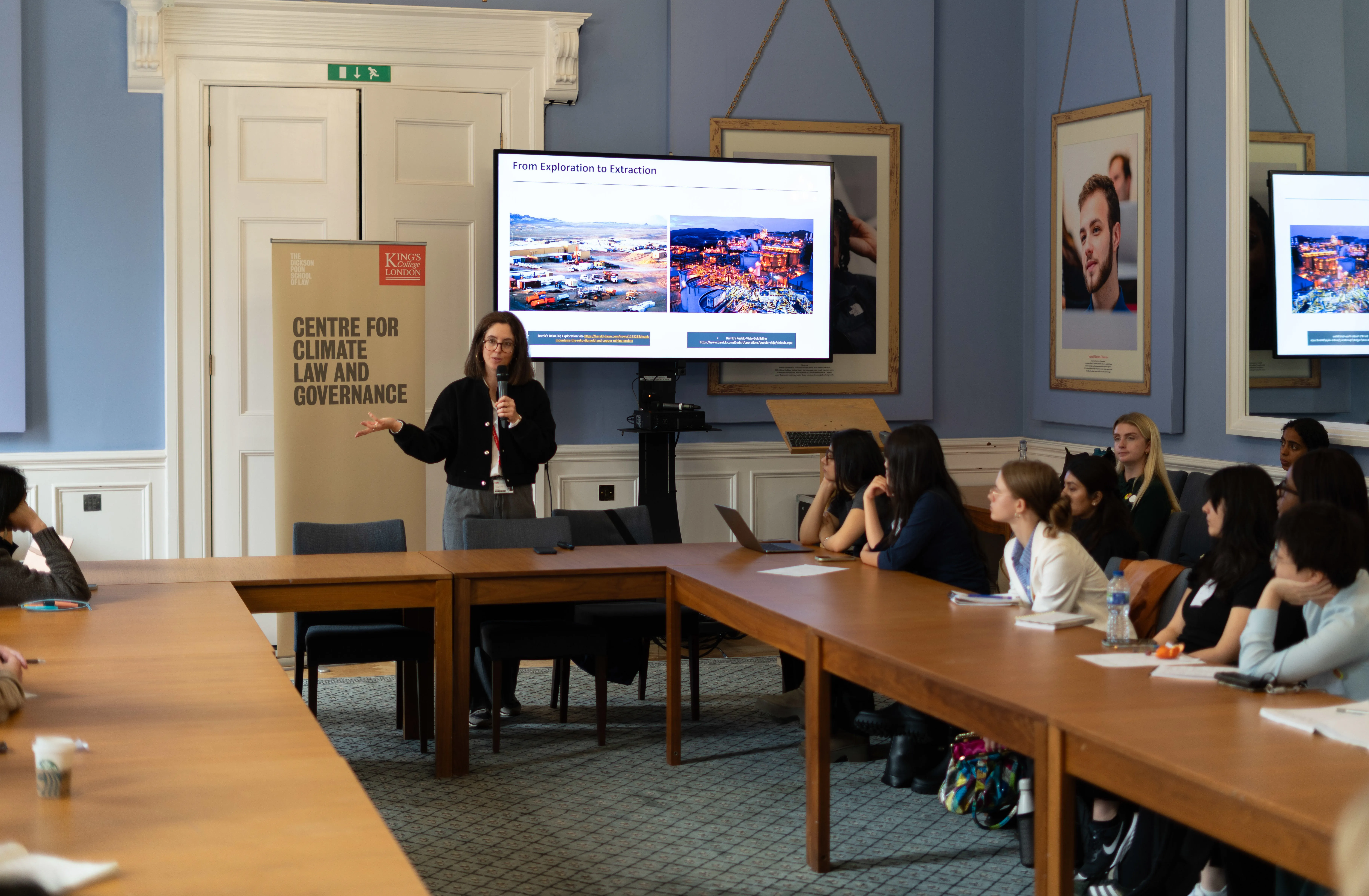 woman speaking to an audience in front of a banner and screen