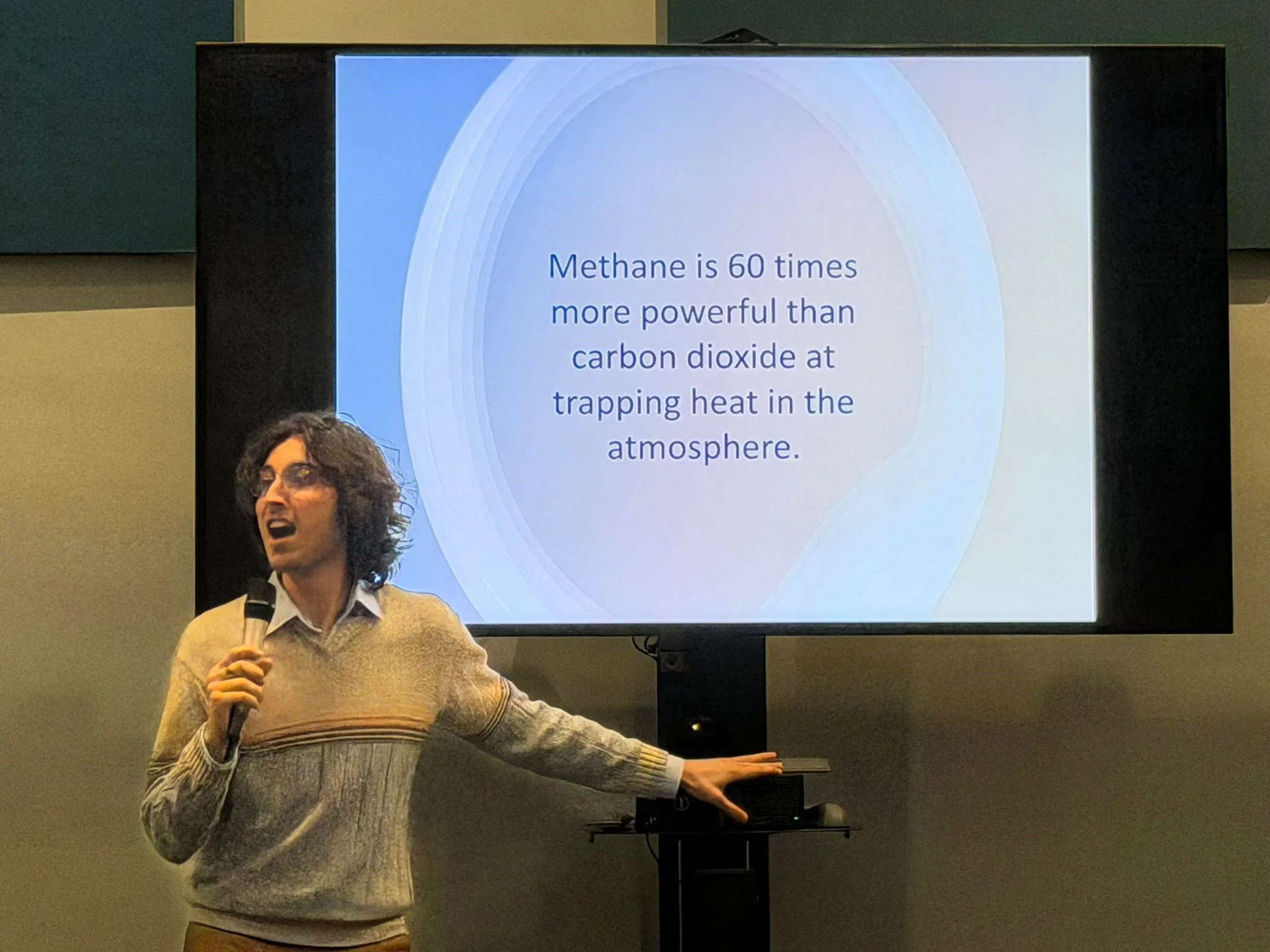 a speaker is speaking at an event with a microphone in front of a projector with writing