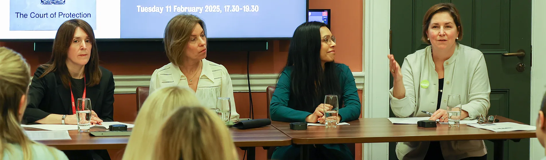 A panel of speakers at a table in front of a presentation