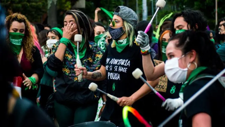 A group of women in black t-shirts and green neckerchiefs join a protest.