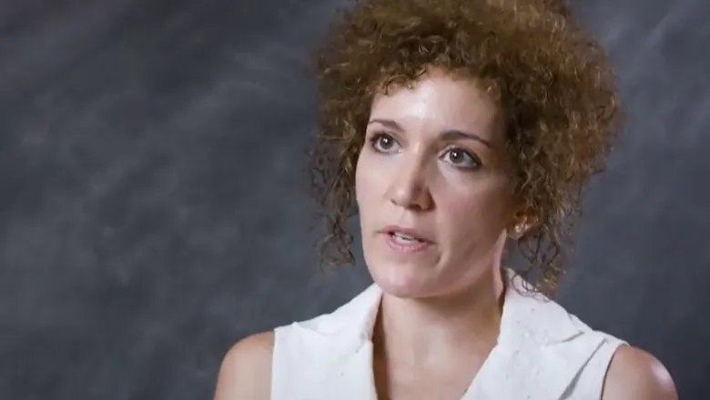 A woman is being interviewed against a grey background