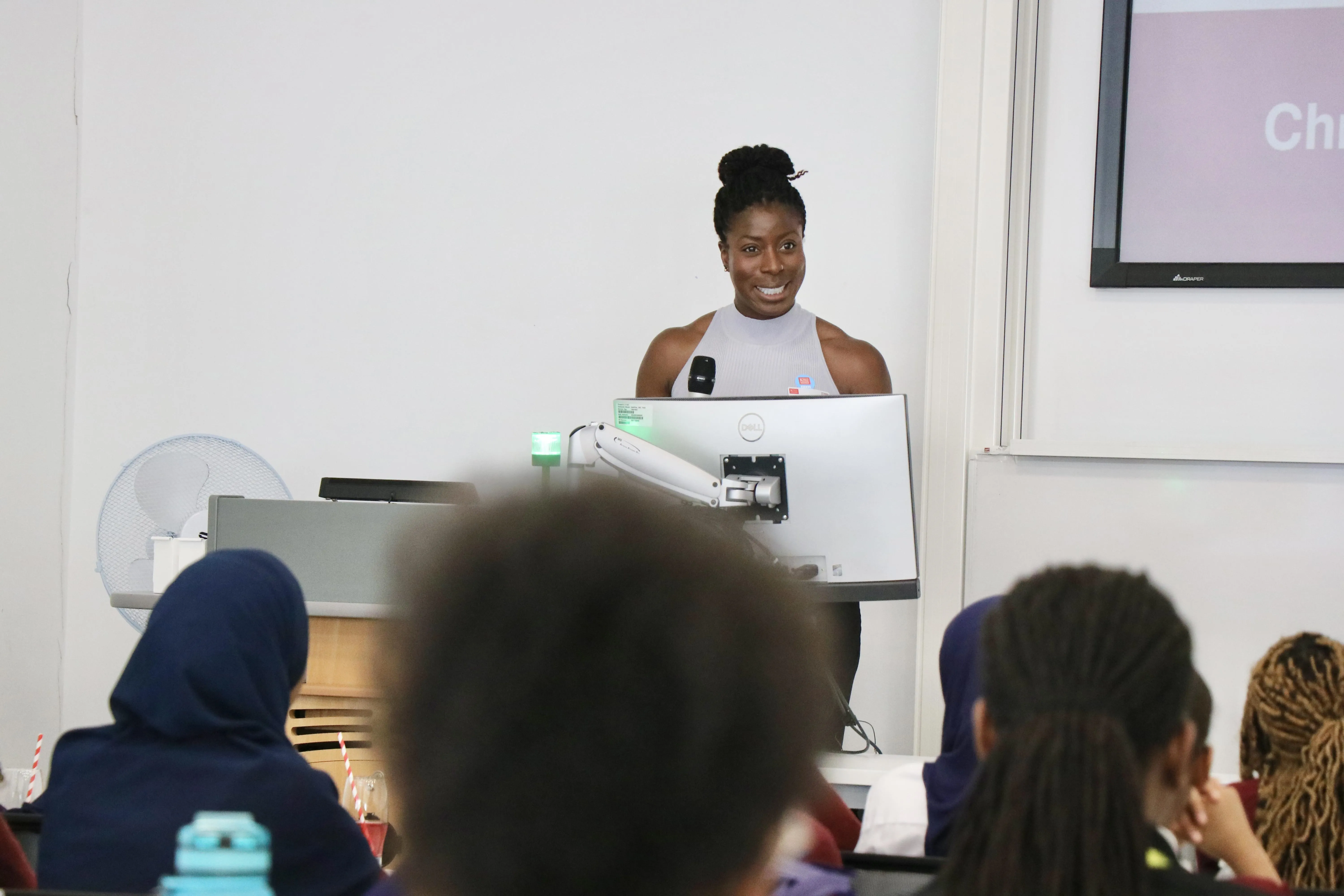 Christine Ohuruogu on stage with a microphone and speaking to the students.