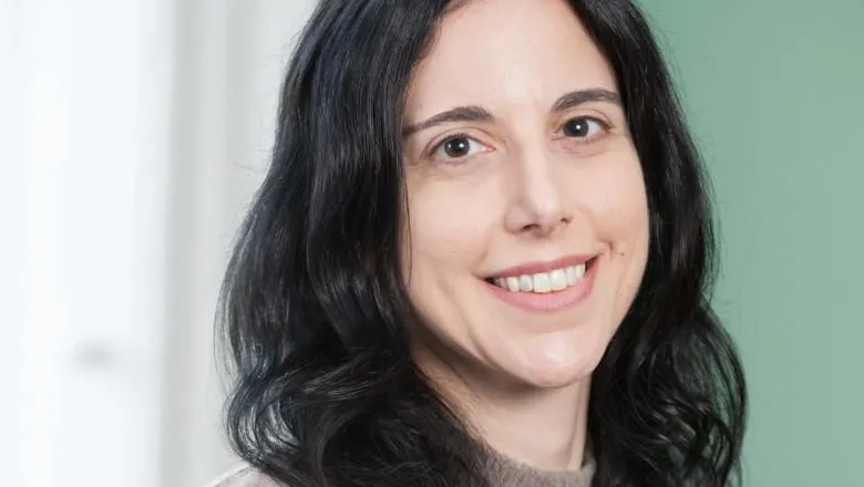 A portrait of a woman with dark hair, smiling, against a white and green background.