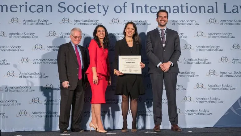 Four people stand on a stage while one receives an award