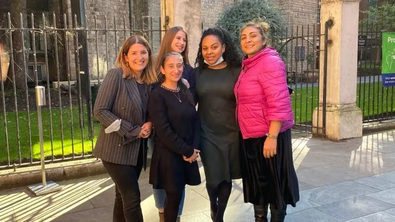 A group of five women, stood in front of a churchyard, smile for the camera.