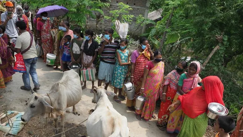 A line of people wait with pans for food.