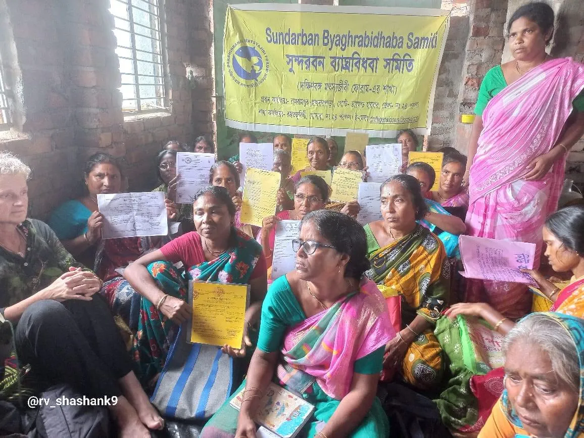 A group of women holding up certificates in a small room with a yellow banner on the wall.