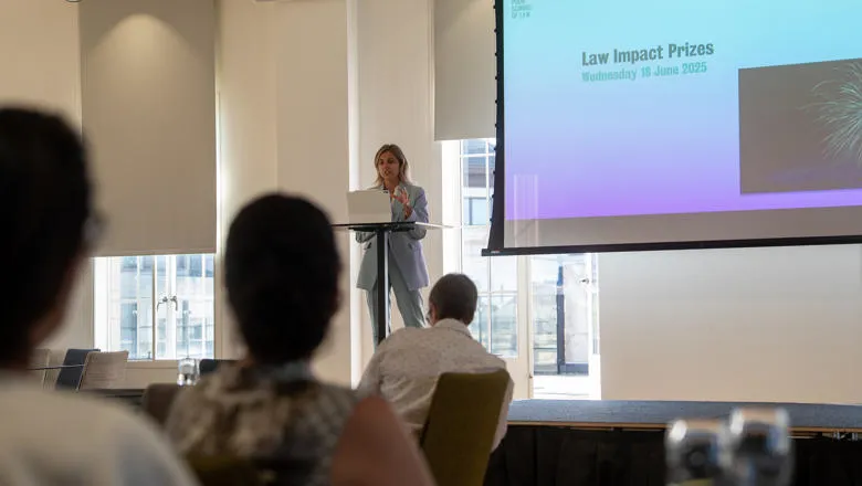 People sitting watching someone speak at a lectern on stage in front of a presentation