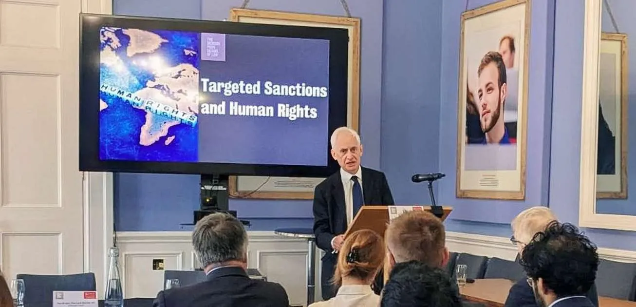 A person speaking from a lectern in front of a presentation
