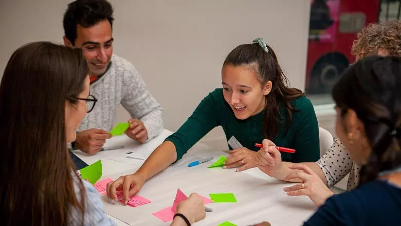 Group of people around a table, writing ideas onto coloured sticky notes