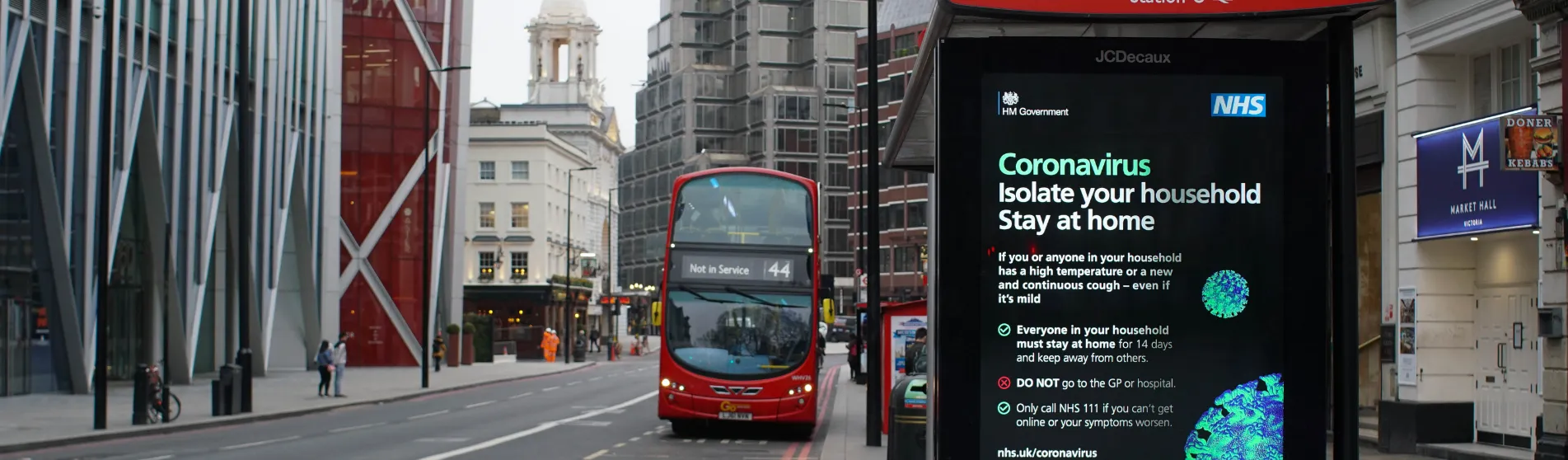 A London bus stop during the COVID-19 pandemic. A London bus approaches a bus stop with a notice saying 'Not in Service'. The bus stop displays a public information poster about coronavirus