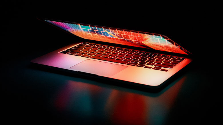 A part open laptop with a colourful screen projecting light onto the keyboard