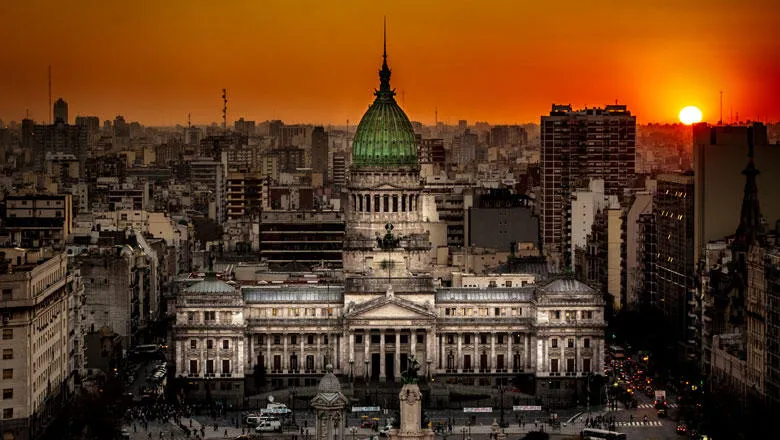 An edited image shows a deep orange sunset over an aerial view of the palatial Argentine National Congress