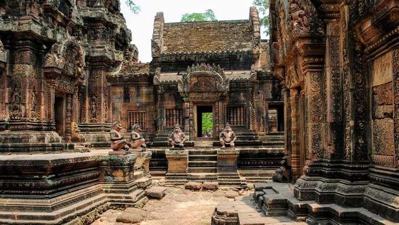 Ruins at Banteay Srei, focused on four ornate humanoid statues