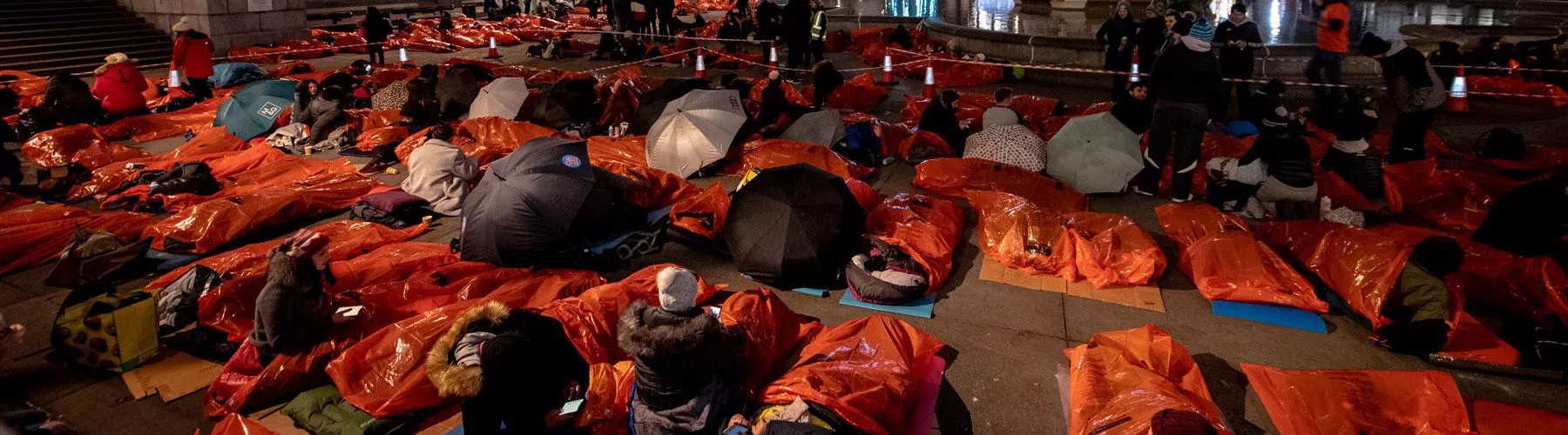 People in orange plastic sleeping bags lie out in Trafalgar Square