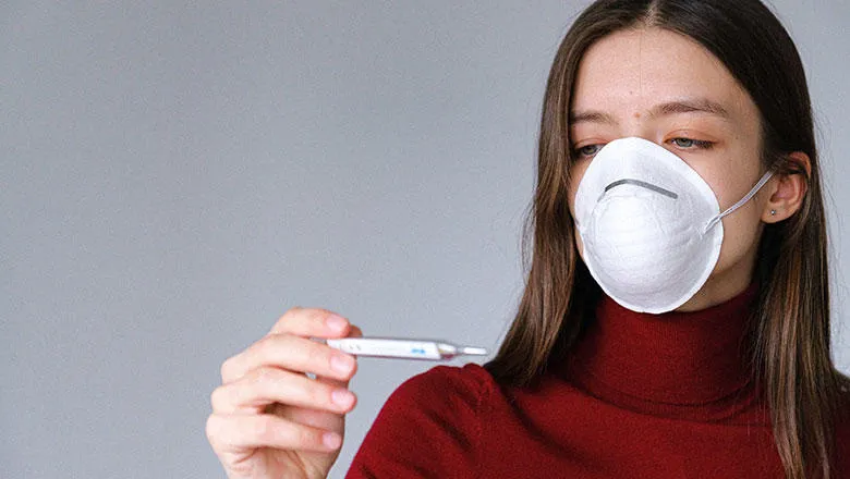 A woman reads a thermometer with a face mask