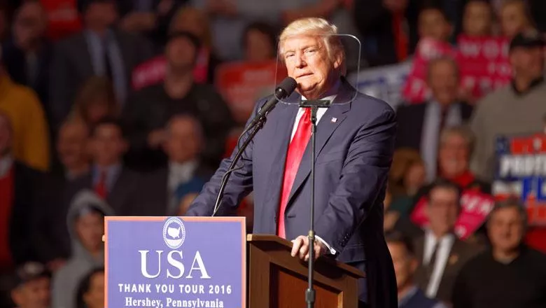 Donald Trump stands at a podium in 2016 on his post-election victory tour