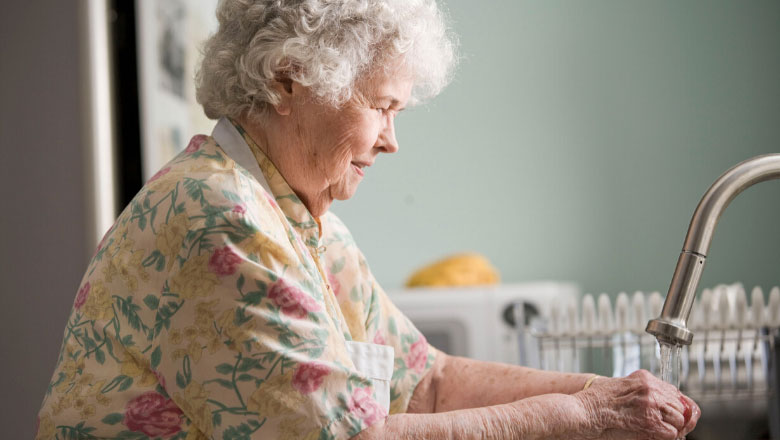 An older woman washes her hands in a sink