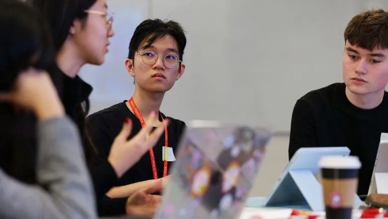 Three students with laptops in discussion.