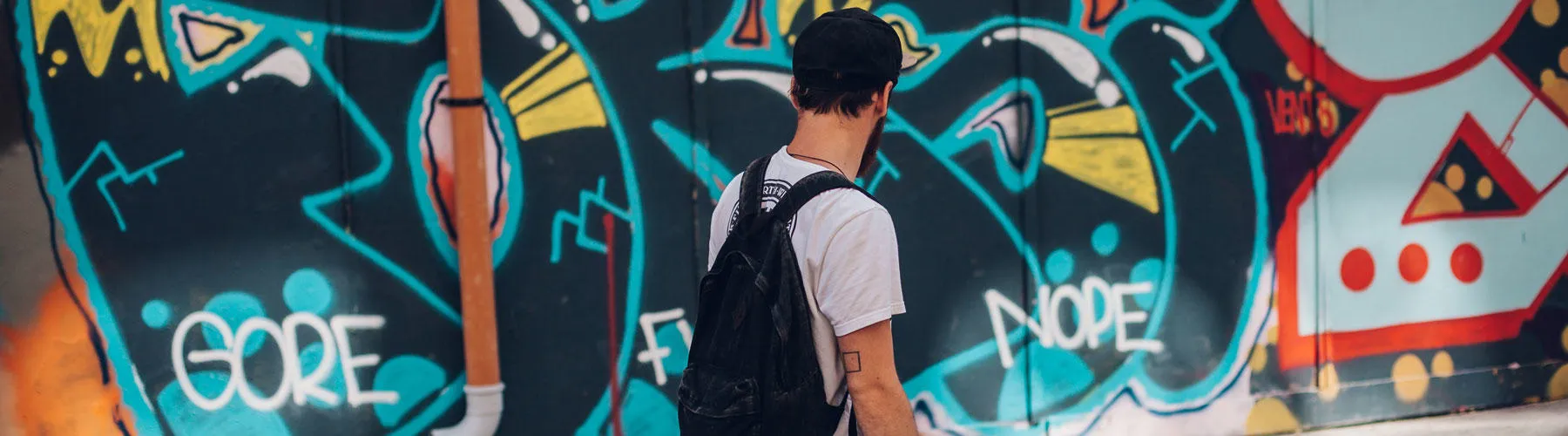 Man with backpack standing in front of graffiti wall