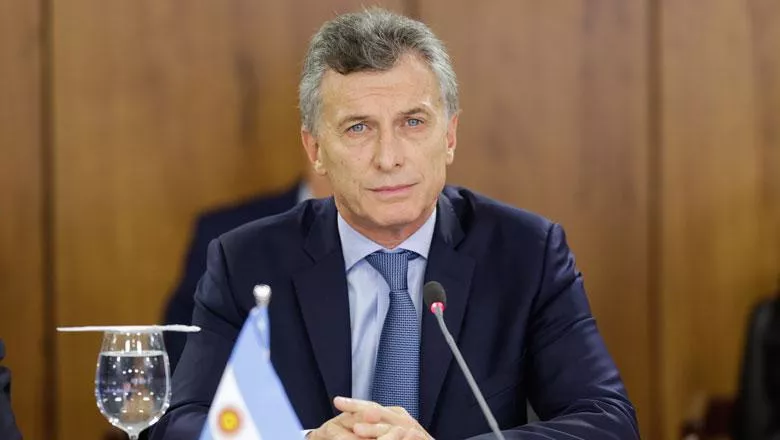 The former president of Argentina Mauricio Macri sits at a conference table behind a small flag and a microphone