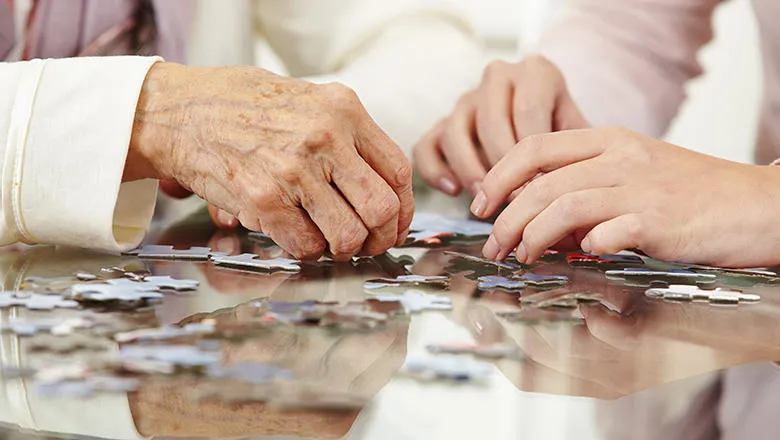 older and younger people's hands over puzzle