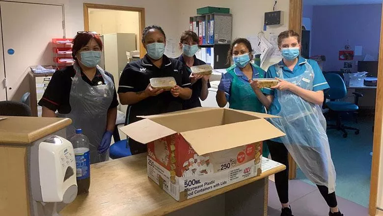 Five medics in face masks stand with food parcels on a ward.