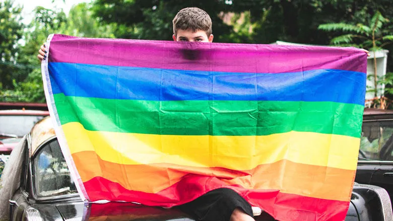 A person hiding their face behind the rainbow flag