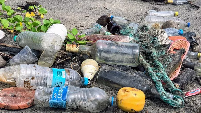 assorted plastic debris and glass bottles on sandy surface