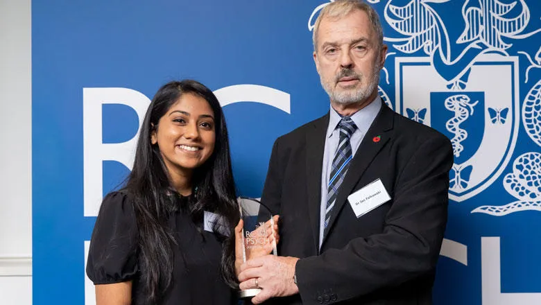 A woman holds a glass award with a man who is presenting it to her