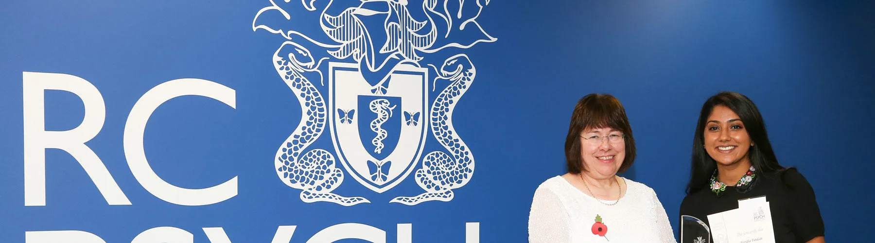 Two people pose in front of the Royal College of Psychiatry logo