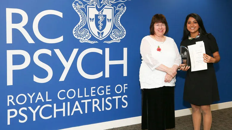 Two people pose in front of the Royal College of Psychiatry logo