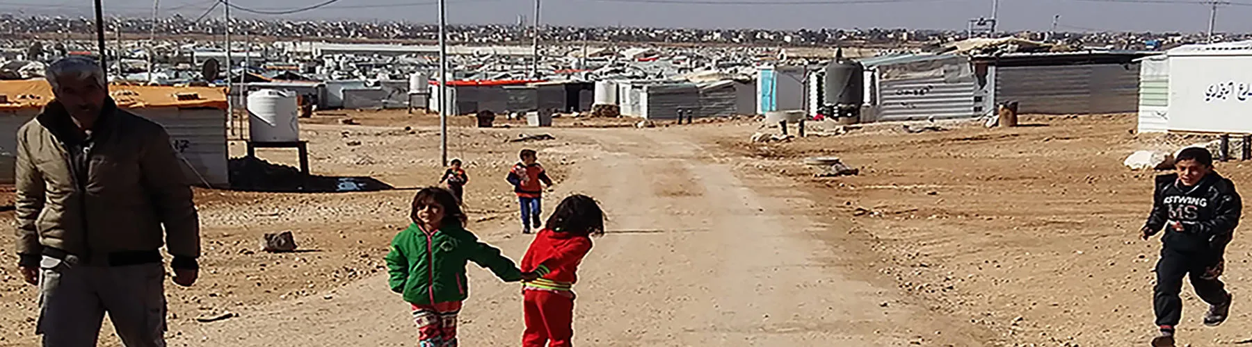 A man and three children on a path, with the camp in the background