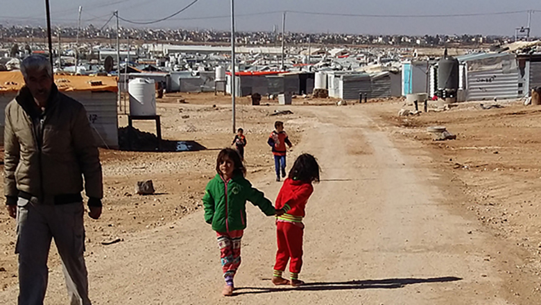 Man and children walking down with refugee camp in background