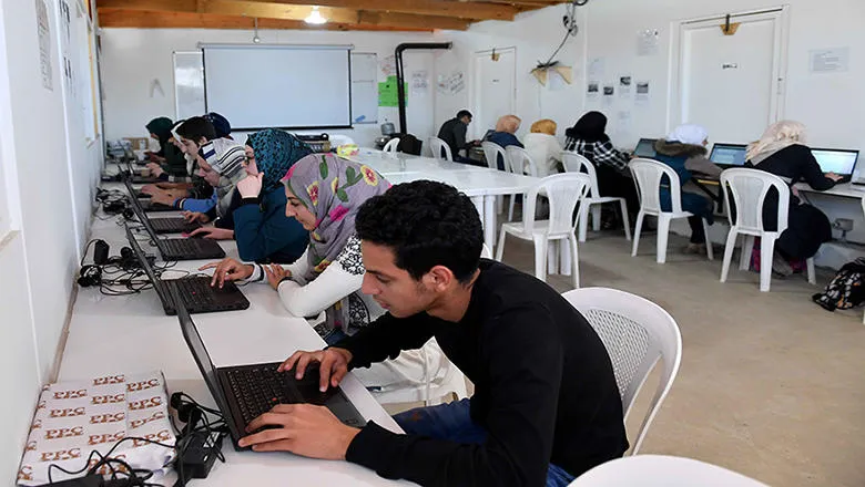 A computer room with people sat on chairs using laptops