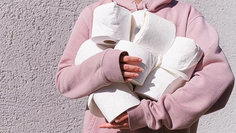A woman in a pink hoody grasps several loo rolls in her folded arms