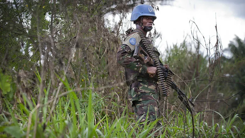 A UN peacekeeper stands in a grassy wooded area in DRC