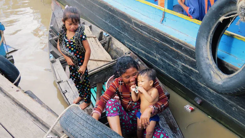 A mother and two young children dock at a pontoon in a small canoe