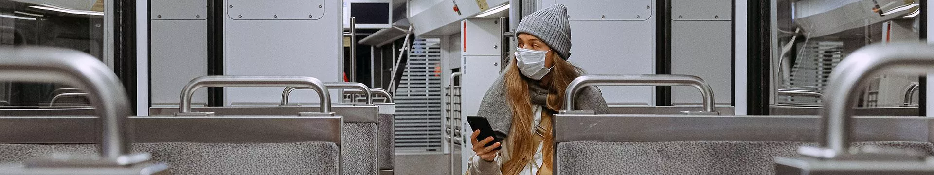 A woman sits alone on a train wearing a face mask