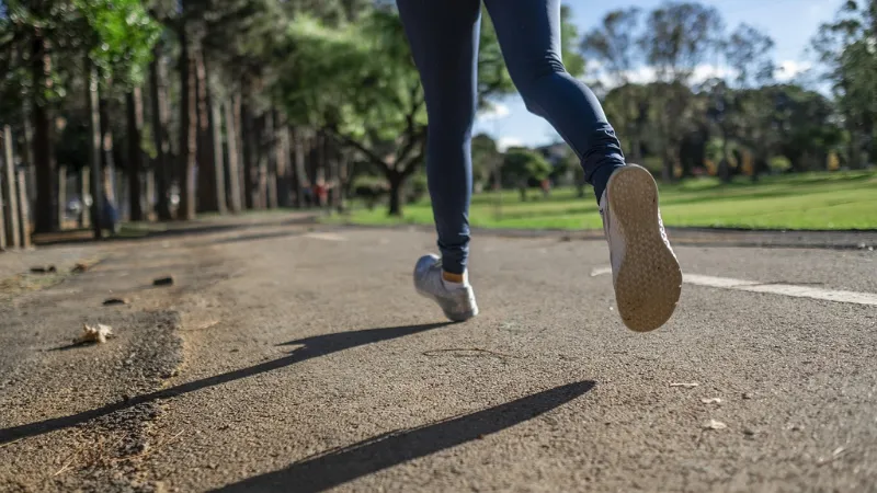 Close-up of a person jogging on a park path surrounded by trees and greenery on a sunny day