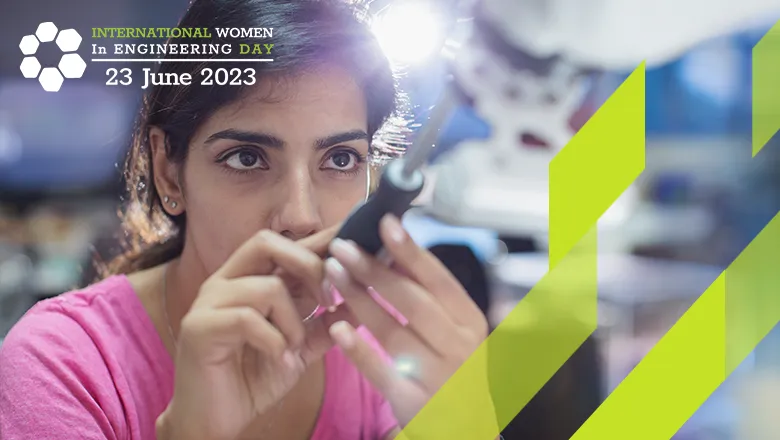 The International Women in Engineering Day logo is displayed over an image of an Asian female engineer adjusting a robotic arm. 