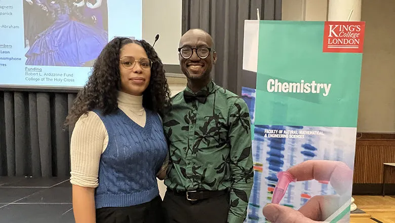 Jhanelle White (L) and Dr André Isaacs (R) stand in front of turquoise 'Chemistry' King's College London banner