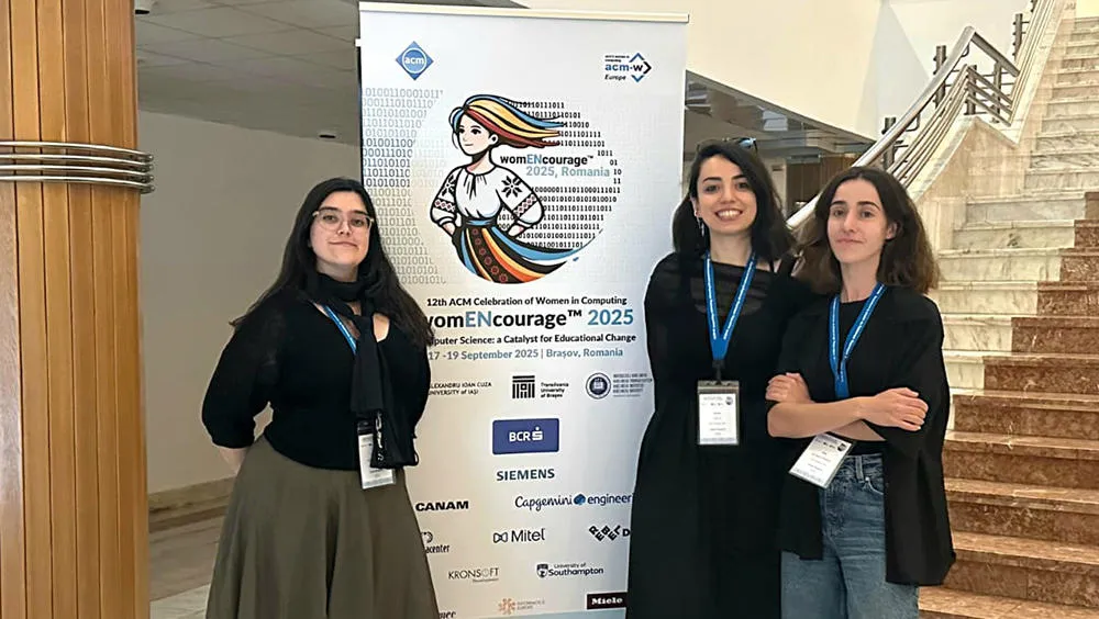 Three PhD student in front of WomENcourage banner